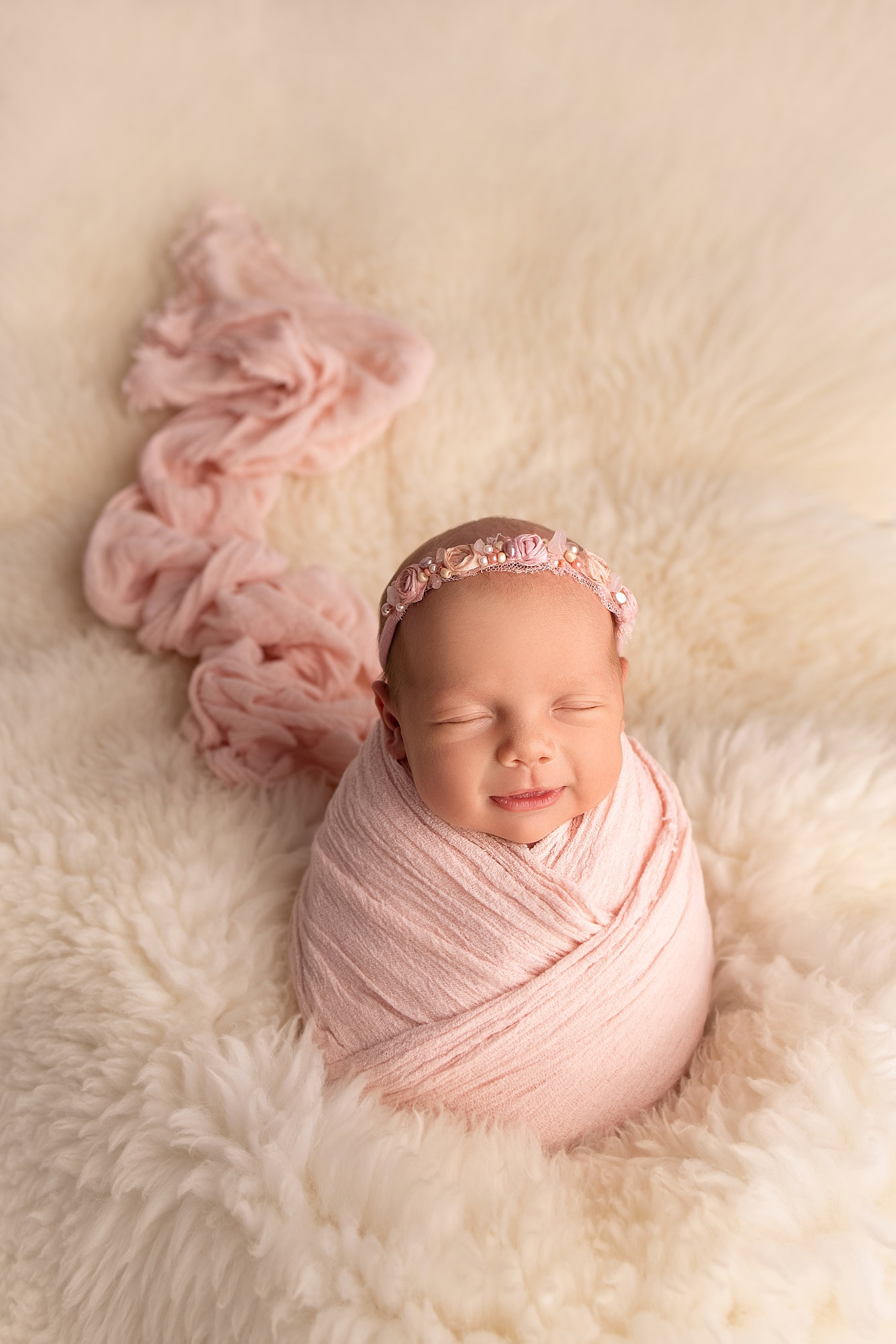 Sleeping newborn girl in a pink cocoon with a pink bandage on a white background